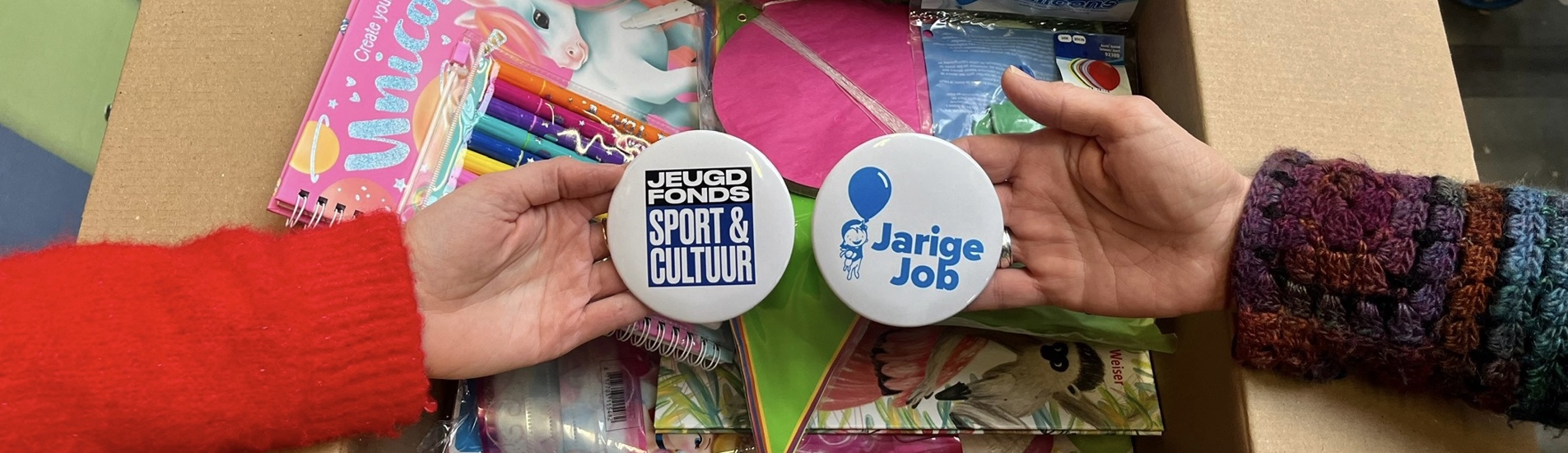 Twee handen houden een Jeugdfonds Sport & Cultuur en Stichting Jarige Job button vast boven verjaardagsbox op loopband